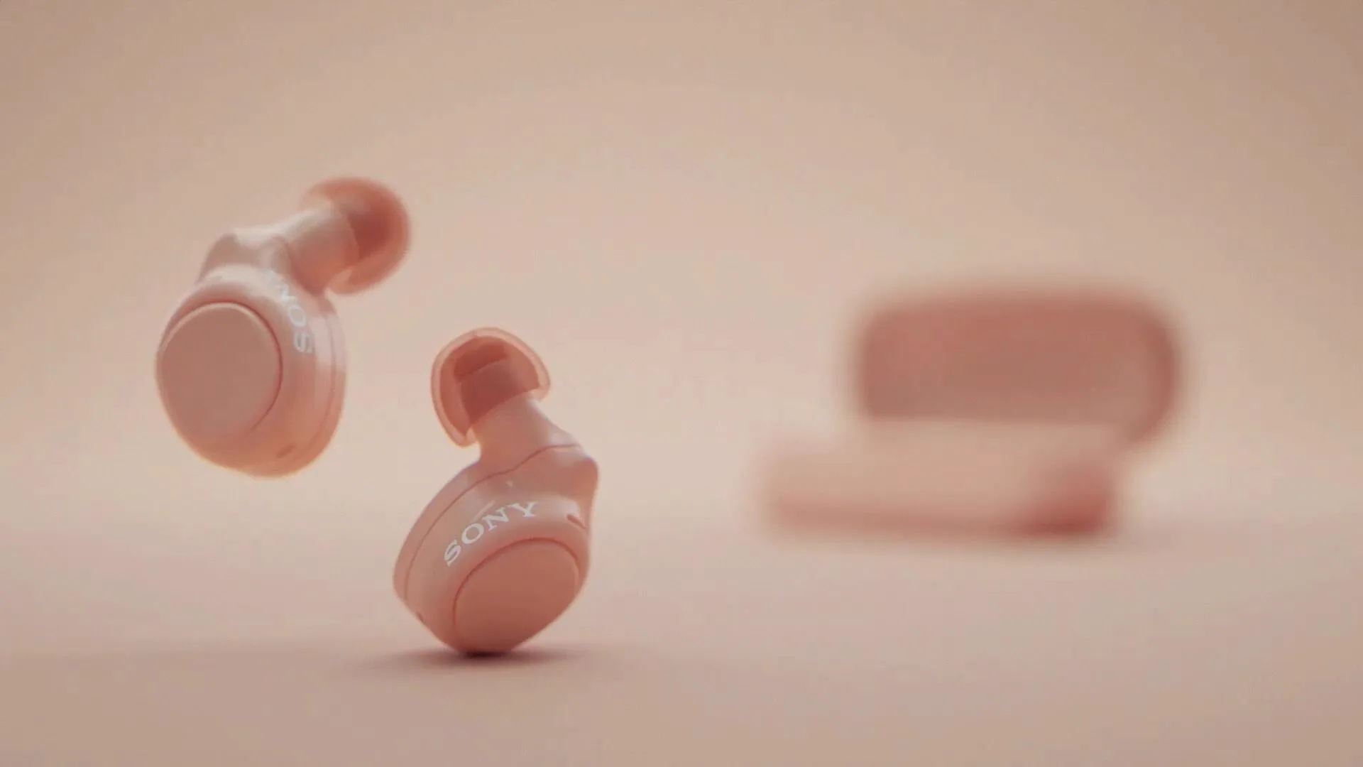 Coral-pink earbuds tumbling against a matching background