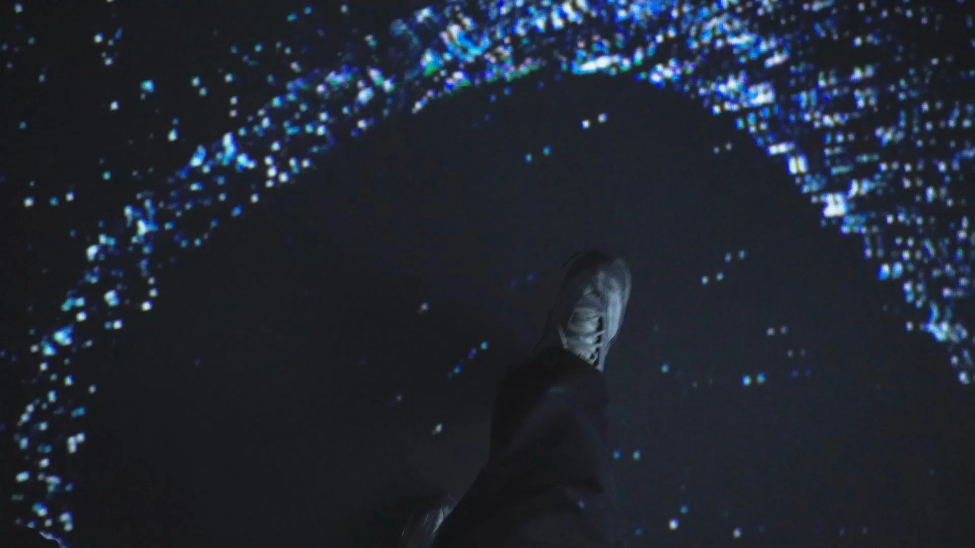 A visitor's foot on the projected floor, a ring of point-cloud particles responding around it